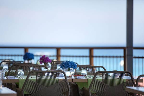 Terrasse des Capo Bay Hotels mit Blick auf das Meer, gedeckte Tische mit Blumenarrangements.