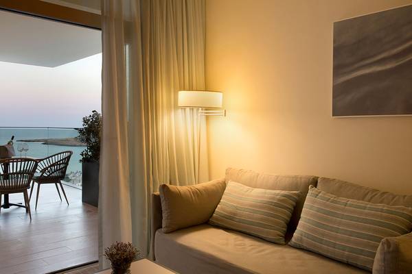 Wohnzimmer mit Meerblick im Capo Bay Hotel, mit einem Sofa, Kissen, Tisch, Stühlen und einer Lampe.