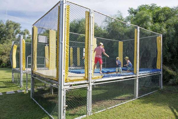 Ein Trampolin-Spielplatz im Freien, umzäunt mit Netzen, mit Kindern, die spielen.