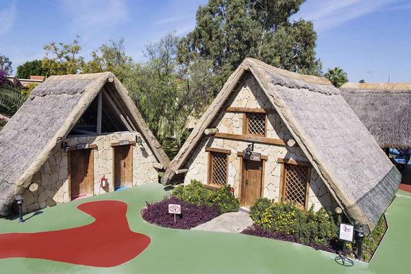 Zwei traditionelle Hütten im Freien mit steinernen Wänden und Strohdächern, umgeben von Pflanzen und einem roten Pfad im Magic Life Belek Hotel.