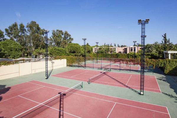 Tennisplätze im Freien im Magic Life Belek Hotel, umgeben von Bäumen und Gebäuden.