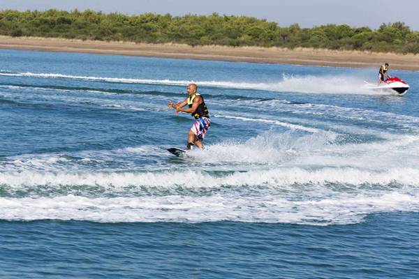 Ein Mann beim Wasserski auf einem Boot, das von einem Jet-Ski gezogen wird.