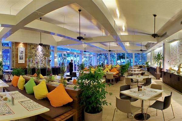 Innenansicht des Restaurants im DoubleTree by Hilton Phuket Banthai Resort mit Tischen, Stühlen, Kissen und Pflanzen.