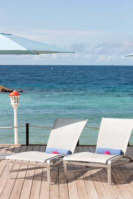 Terrasse des Avila Beach Hotels mit zwei Liegen und geöffneten Sonnenschirmen am Meer.