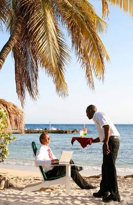 Ein Mitarbeiter des Avila Beach Hotels serviert einem Gast auf dem Strand einen Laptop mit Getränken.