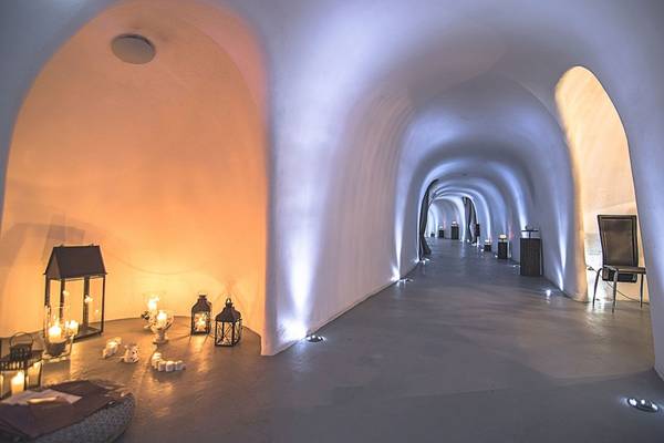 Ein unterirdischer Korridor im Ambassador Aegean Luxury Hotel & Suites, mit runden Gewölben, weißen Wänden und mehreren brennenden Kerzen.