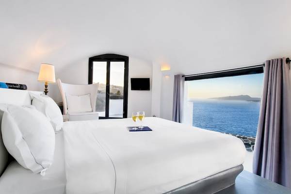 Luxuriöse Suite im Ambassador Aegean Luxury Hotel mit Meerblick, Bett, Weinglas und offenem Fenster.