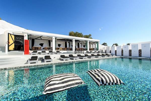 Poolbereich des Ambassador Aegean Luxury Hotel mit weißen Sonnenliegen und schwarzen Kissen.