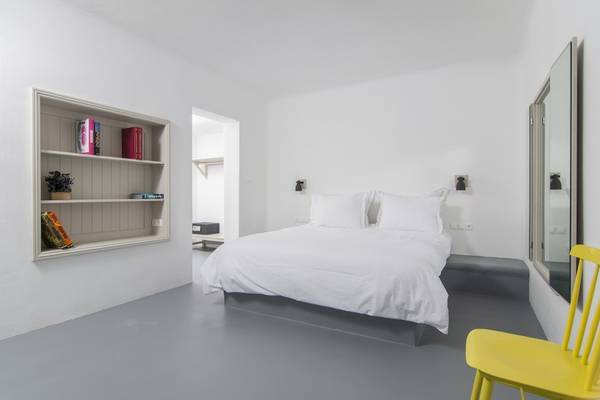 Schlafzimmer mit Bett, Schrank, Lampe und gelbem Stuhl