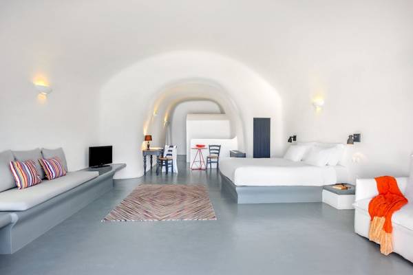 Innenraum des Ambassador Aegean Luxury Hotel & Suites mit weißem Bett, grauem Boden und heller Einrichtung.