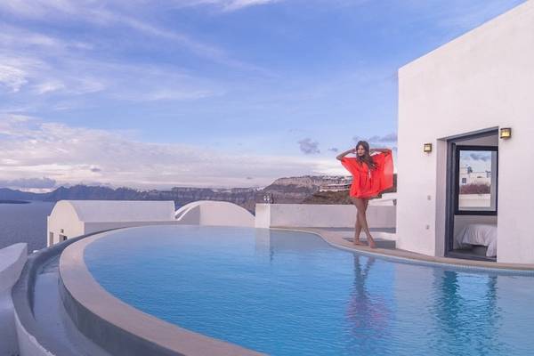 Eine Frau in einem roten Kleid steht neben dem Pool des Ambassador Aegean Luxury Hotel & Suites mit Blick auf das Meer.