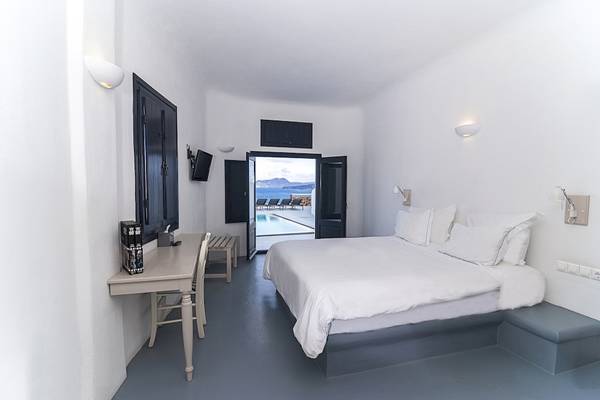 Innenansicht einer Suite im Ambassador Aegean Luxury Hotel mit weißem Bett, Schreibtisch und Poolblick.