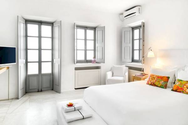 Schlafzimmer im Ambassador Aegean Luxury Hotel mit weißem Bett und Möbeln, zwei Fenstern und Klimaanlage.