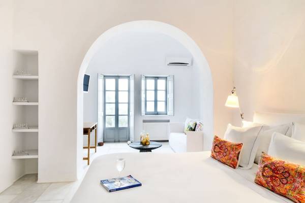 Innenansicht eines Schlafzimmers im Ambassador Aegean Luxury Hotel & Suites mit weißen Wänden, einem großen Bett und einem Schreibtisch.