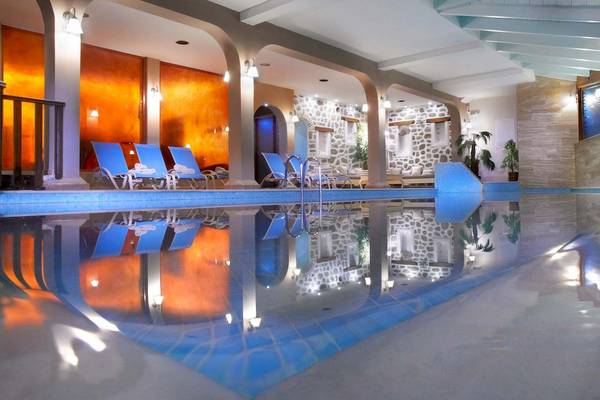 Poolbereich im Acrotel Athena Pallas Hotel mit blauen Liegestühlen und Steinwänden.
