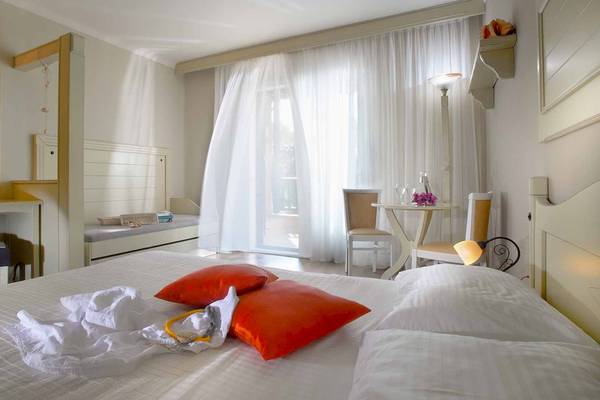 Das Hotelzimmer im Acrotel Athena Pallas mit einem Bett, roten Kissen, weißem Laken, einem Tisch und Stühlen.