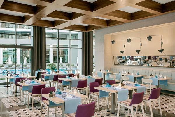 Innenansicht des Restaurants im Acanthus Cennet Barut Collection Hotel mit blauen Tischen und Stühlen.