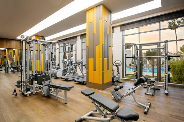 Innenansicht des Fitnesscenters im Acanthus Cennet Barut Collection Hotel mit verschiedenen Trainingsgeräten und einer Poolansicht.