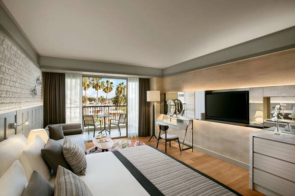 Innenansicht eines Hotelzimmers mit Bett, Schreibtisch, Fernseher und Balkon.