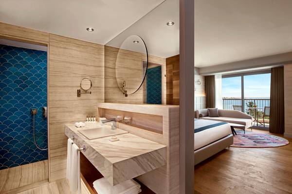 Innenansicht eines Hotelzimmers mit Badezimmer und Schlafzimmerbereich, Blick auf den Balkon.
