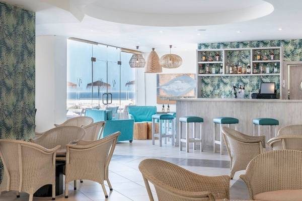 Innenansicht des Vincci Tenerife Golf Hotels mit Bar, Stühlen und Tischen, tropischen Mustern an den Wänden und Blick auf das Meer.