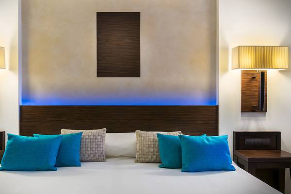 Innenansicht eines Hotelzimmers im Elysium Resort & Spa mit einem Bett, blauen Kissen und blauen Lampen an der Wand.