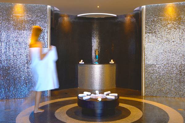 Eine Frau in einem weißen Handtuch steht vor einer Wellnesskabine im Elysium Resort & Spa.