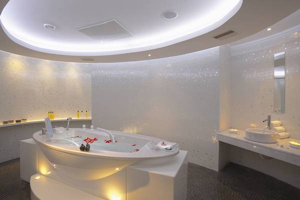 Innenansicht des Badezimmers im Elysium Resort & Spa mit einer großen Badewanne, beleuchteten Wänden und einem Waschbecken.