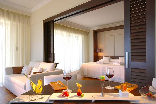 Innenansicht der Suite im Elysium Resort & Spa mit Bett, Couch und Tisch mit Wein und Essen.