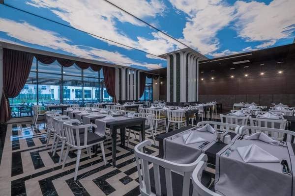 Innenansicht des Restaurants im Adalya Elite Lara Hotel mit Tisch und Stuhl-Arrangements unter einer Deckenprojektion.