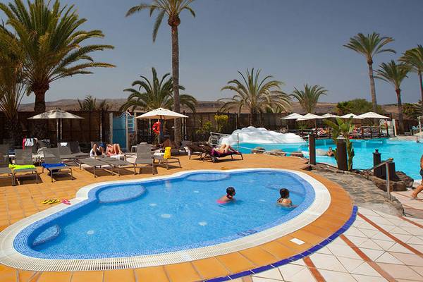Außenpoolbereich des Abora Continental Hotels mit Liegestühlen, Sonnenschirmen und Palmen.