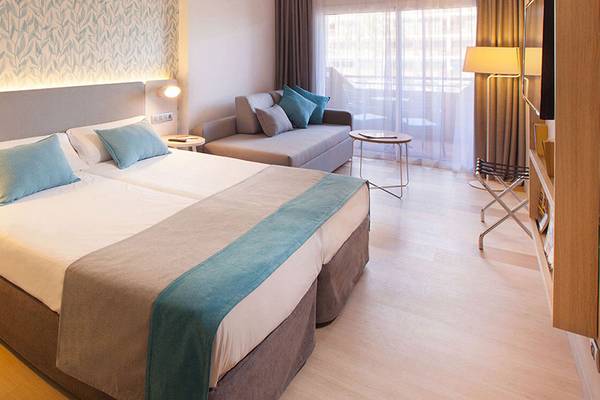 Ein modernes Hotelzimmer im Abora Continental by Lopesan mit zwei Betten, einer Couch, Tisch, Lampe und Telefon.