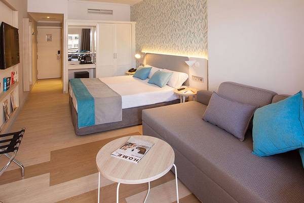 Innenansicht eines Zimmers im Abora Continental by Lopesan Hotel mit Bett, Sofa und Zeitschriftentisch.