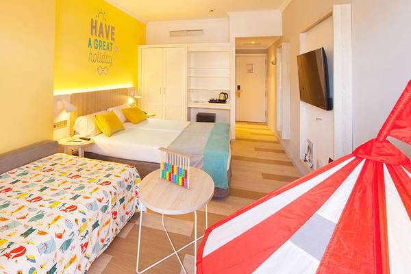 Zimmer im Abora Continental by Lopesan mit zwei Betten, buntem Bettzeug und gelber Wand mit Aufschrift.