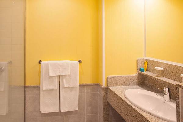 Badezimmer des Abora Continental by Lopesan Hotels mit gelben Wänden, Glasdusche und Waschbecken.