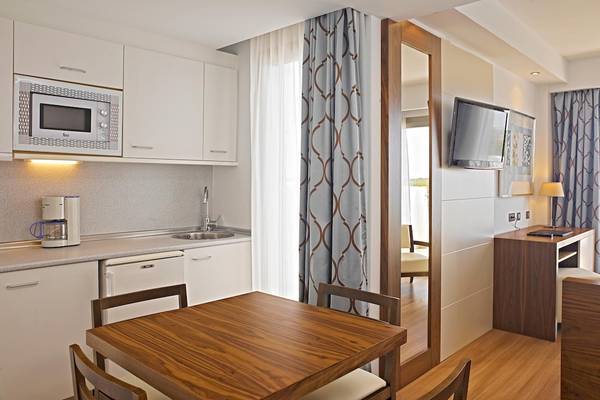 Innenansicht eines Zimmers im Hipotels Cala Millor Park Hotel mit Küchenbereich, Tisch und Fernseher.