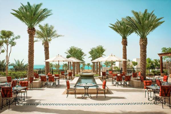 Außenbereich des St. Regis Saadiyat Island Resorts mit Tischen, Stühlen und Palmen