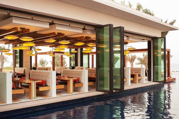 Poolside-Restaurant im St. Regis Saadiyat Island Resort mit offenen Glastüren und Tischen.