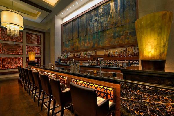 Bar im St. Regis Saadiyat Island Resort mit Barhockern, Theke und dekorativen Wandleuchten.