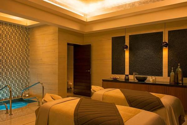 Behandlungsraum im Spa des St. Regis Saadiyat Island Resort mit zwei Massageliegen, einem kleinen Pool und einem Eingang.