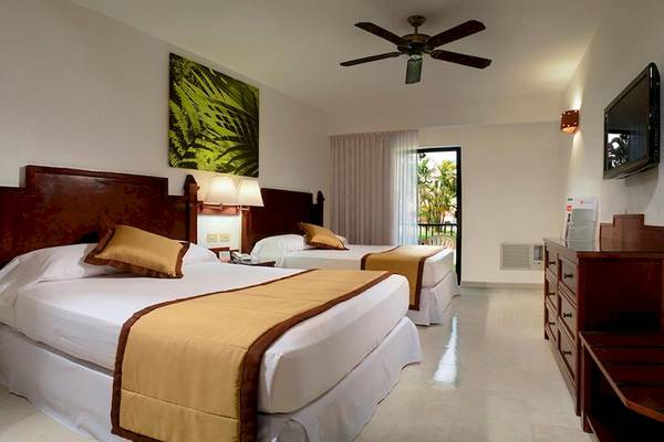 Zwei Doppelzimmer im Riu Lupita Hotel mit Betten, Decken, Kissen, Deckenventilator, Fernseher und Nachttisch.