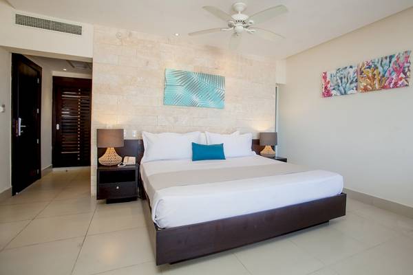 Innenansicht eines Schlafzimmers im Vista Sol Punta Cana Beach Resort & Spa mit einem Doppelbett, Nachttischen und Kunstwerken an der Wand.