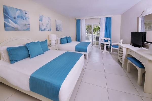 Innenansicht eines Doppelzimmers im Vista Sol Punta Cana Beach Resort & Spa mit zwei Betten, blauen Kissen und einem Balkon.
