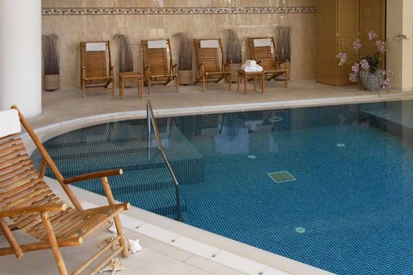 Innenpool des Aquila Porto Rethymno Hotels mit Holzstühlen und Handläufen.