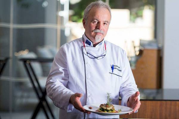 Chef des Aquila Porto Rethymno präsentiert ein Gericht in einem weißen Kochmantel.