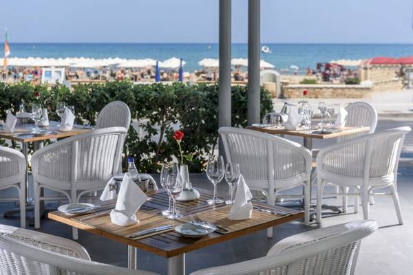 Außensitzbereich des Aquila Porto Rethymno Hotels mit weißen Tischen und Stühlen am Meer.