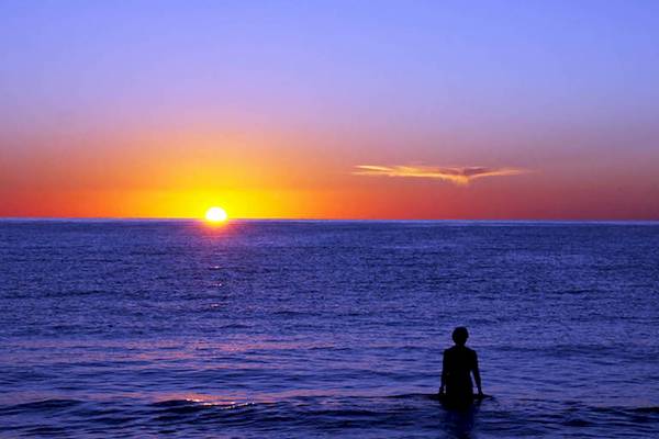 Ein Mensch steht im Meer und beobachtet den Sonnenuntergang.