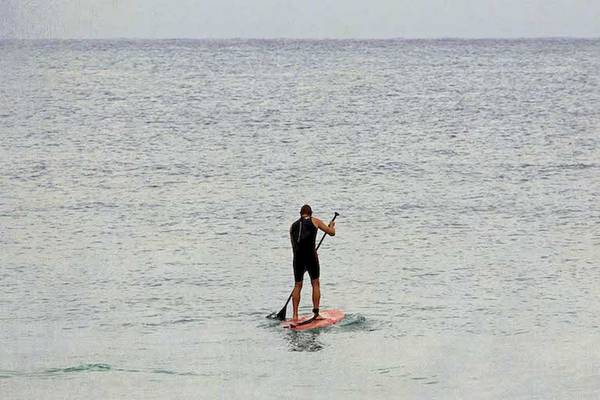 Ein Mann steht auf einem roten Surfbrett und paddelt auf dem offenen Meer.
