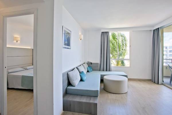 Innenansicht eines Zimmers im Playa Dorada Aparthotel mit Doppelbett, Sofa und Fenstern.