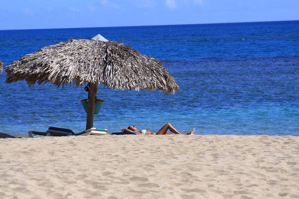 Eine Frau liegt auf dem Strand unter einem Strohhut mit Blick auf das Meer.